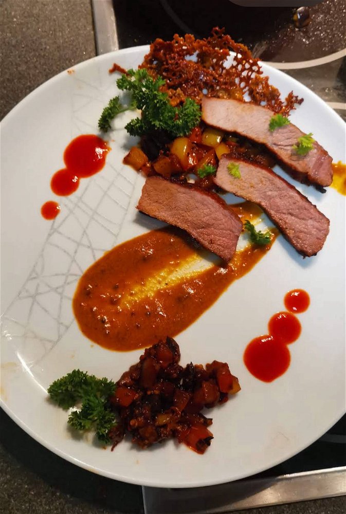 Wildschwein Nackensteak mit gebratenen Gemüse Brunoise, frischer Petersilie an Pfefferrahmsauce. Garniert mit Sriracha und einer Rahmkoralle