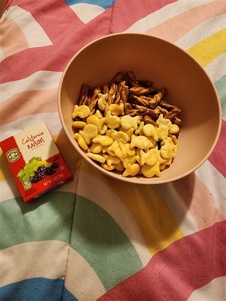 Goldfish snacks and pretzels in a pink bowl. A small box of raisins.