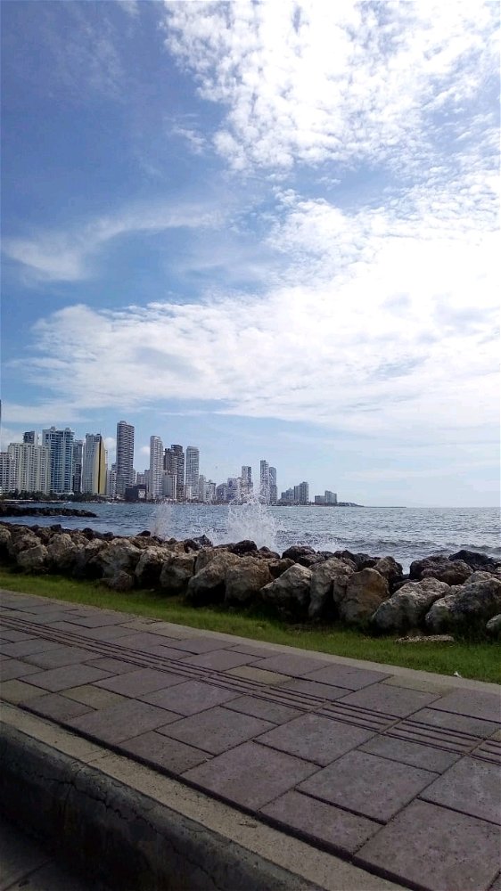 Cielo azul, nubes dispersas, viento frío, agua salpicando en olas a la playa, ciudad Cartagena de Indias, Colombia 